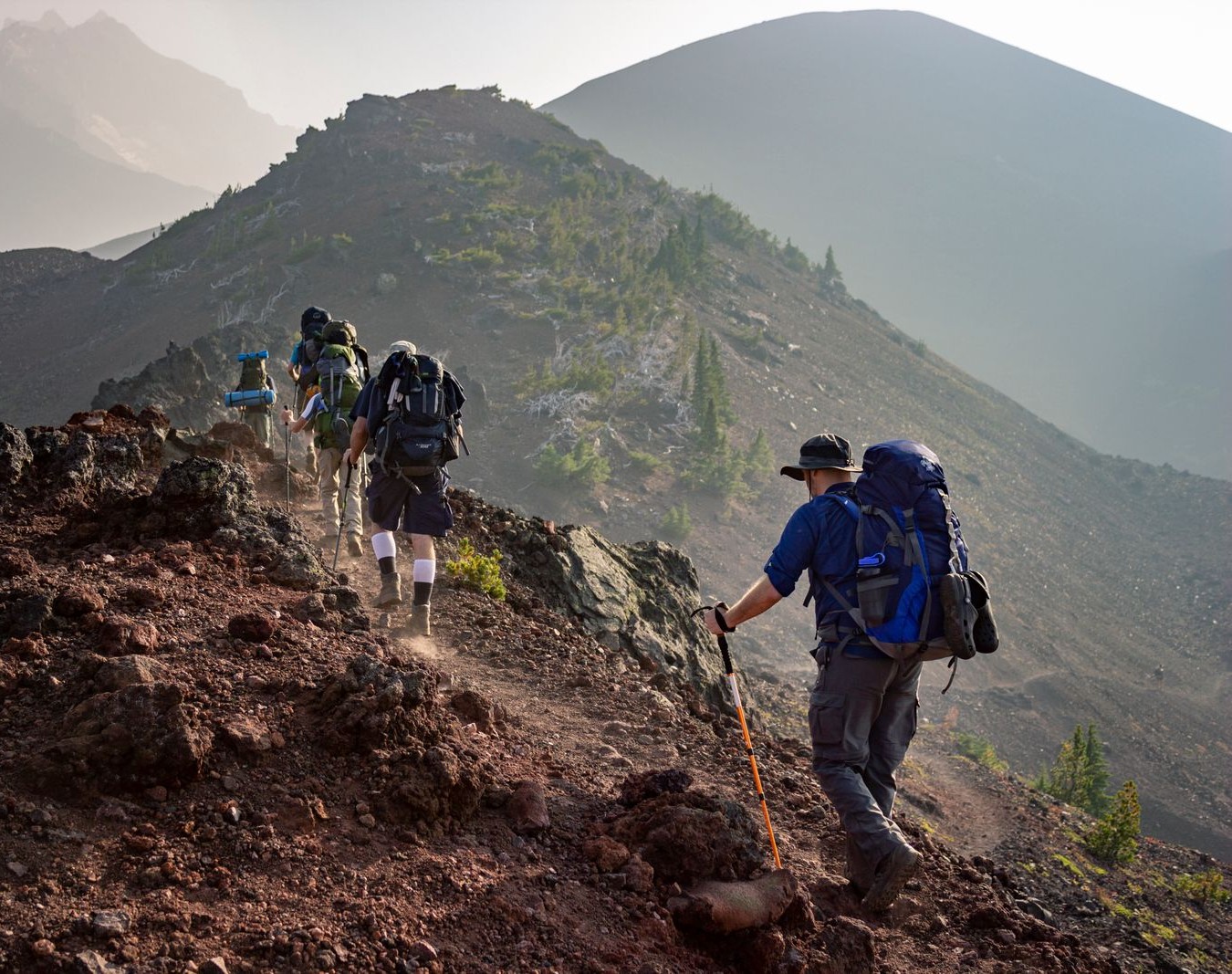 Group of hikers with backpacks walking along a rocky mountain ridge trail